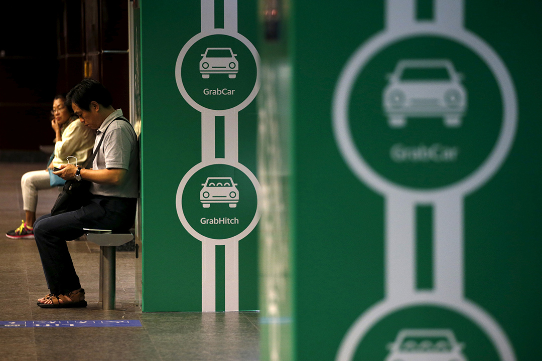 Commuters wait for a train next toGrab transport booking service app advertisements at a train station in Singapore